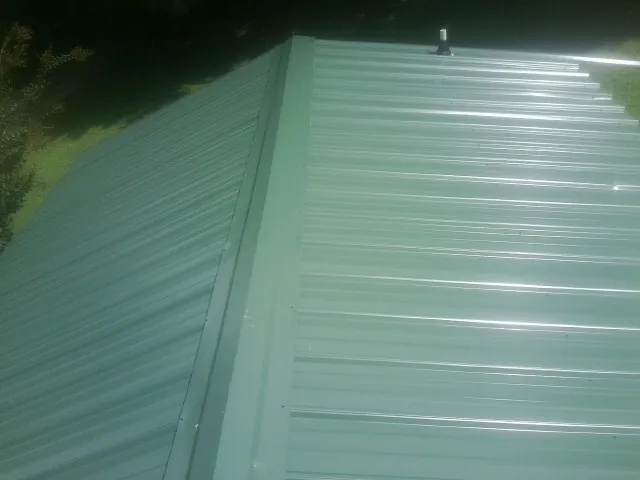 New green metal panels meeting at the ridge of a roof — Flat Roof Repair work by our crew in Loudon