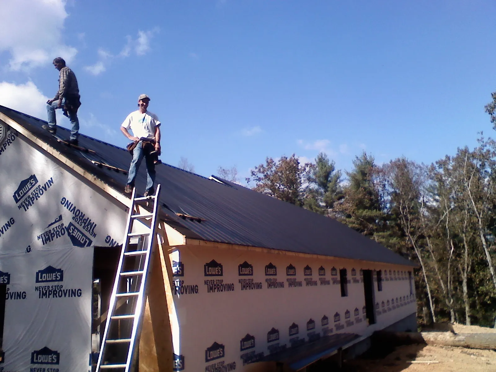 Two roofers standing on a long dark metal roof over a wrapped building in Loudon