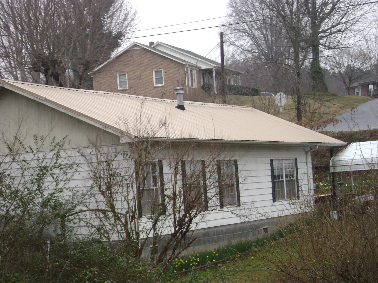 Tan metal roof on a white sided house set into a hillside — Commercial Roofing by Roofing Brothers in Loudon