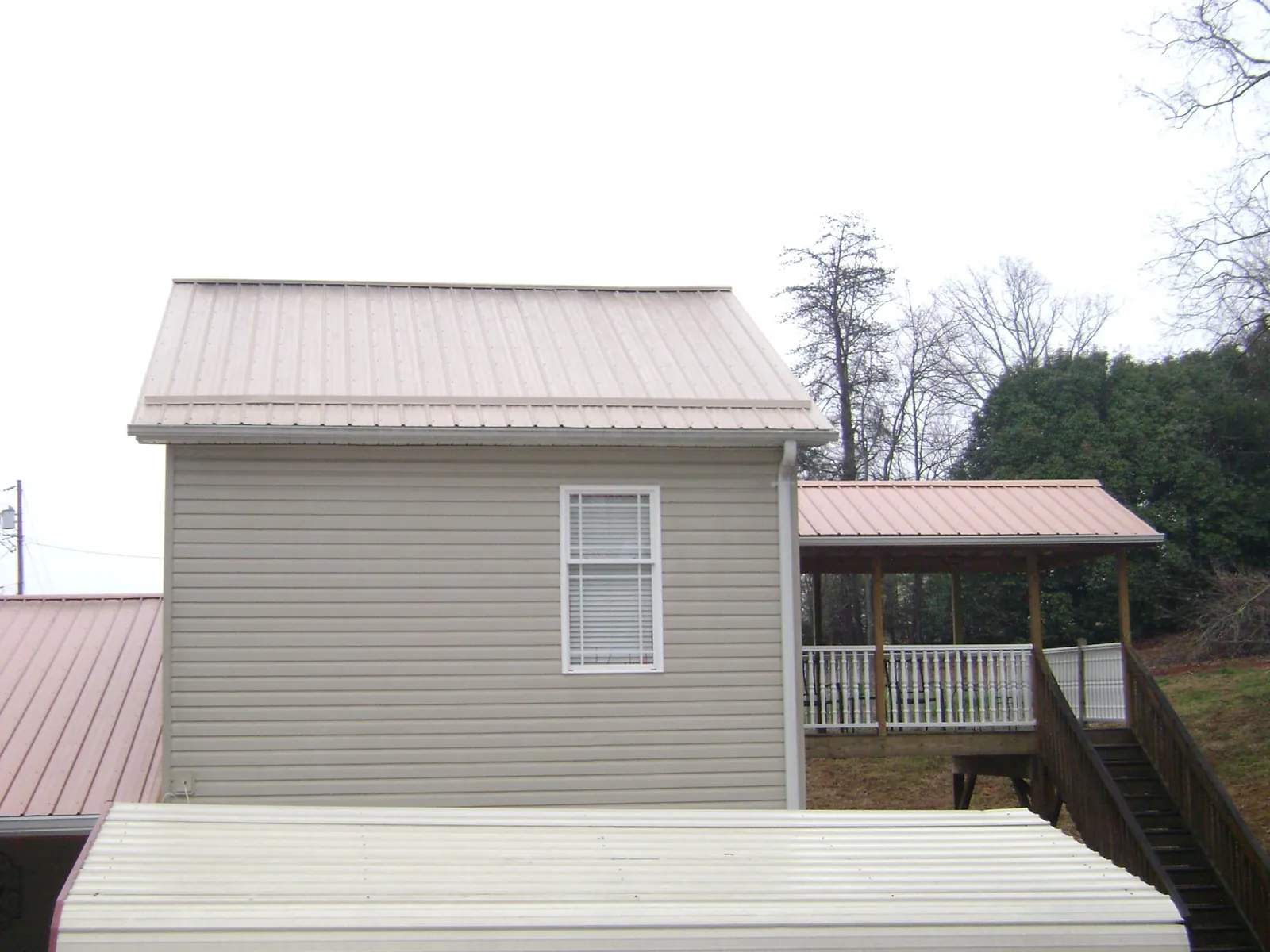 Tan metal roofs on a two story addition and attached porch, from a Roof Replacement job in Loudon